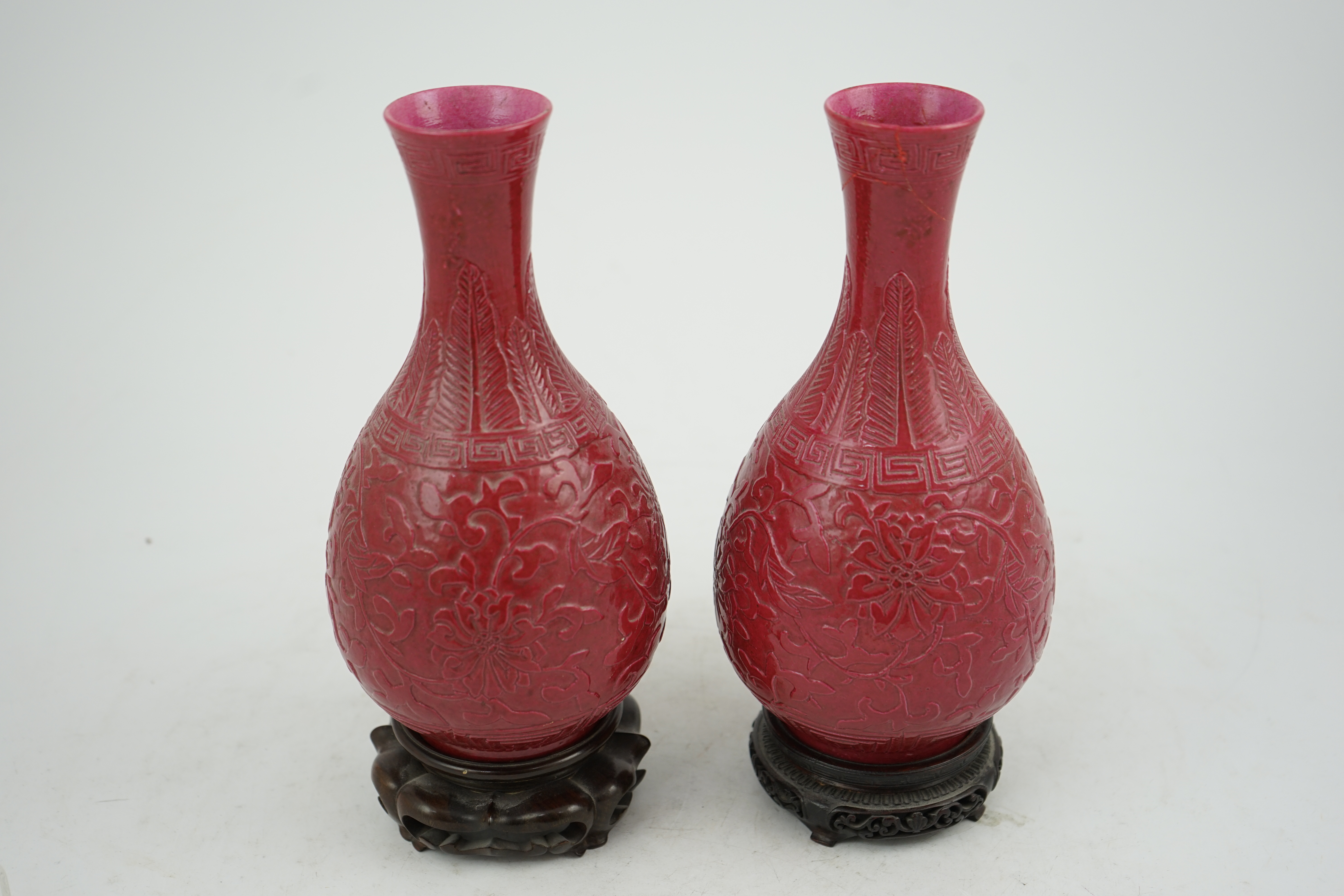 A pair of Chinese ruby ground ‘lotus’ bottle vases, late 19th century, each carved in relief with lotus flowers, scrolling tendrils and leaves, both with carved stands, 24cm high. Condition - one vase the neck broken bot